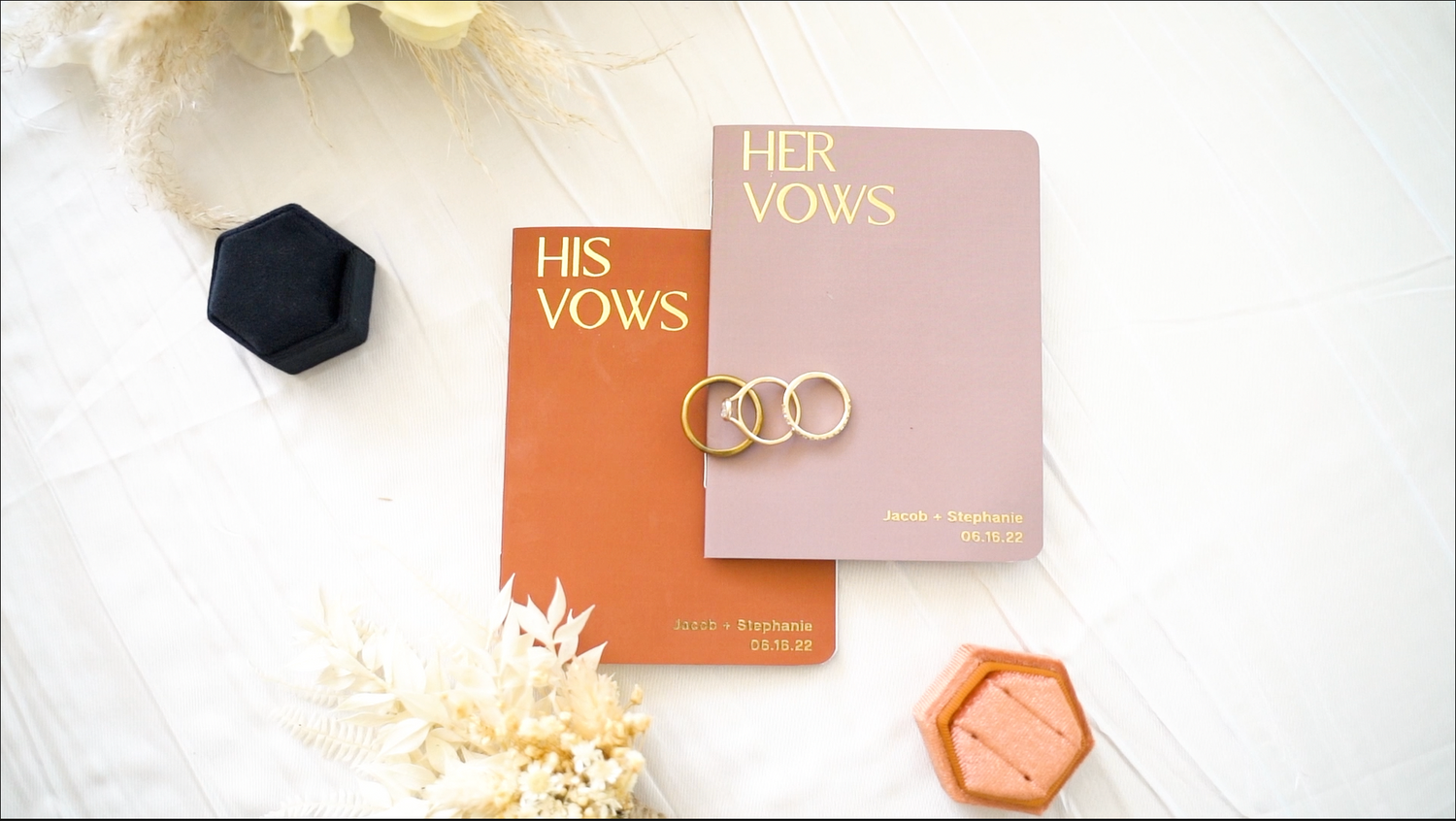 Minimalist flat lay of wedding vow books and decorative elements in orange and pink tones.