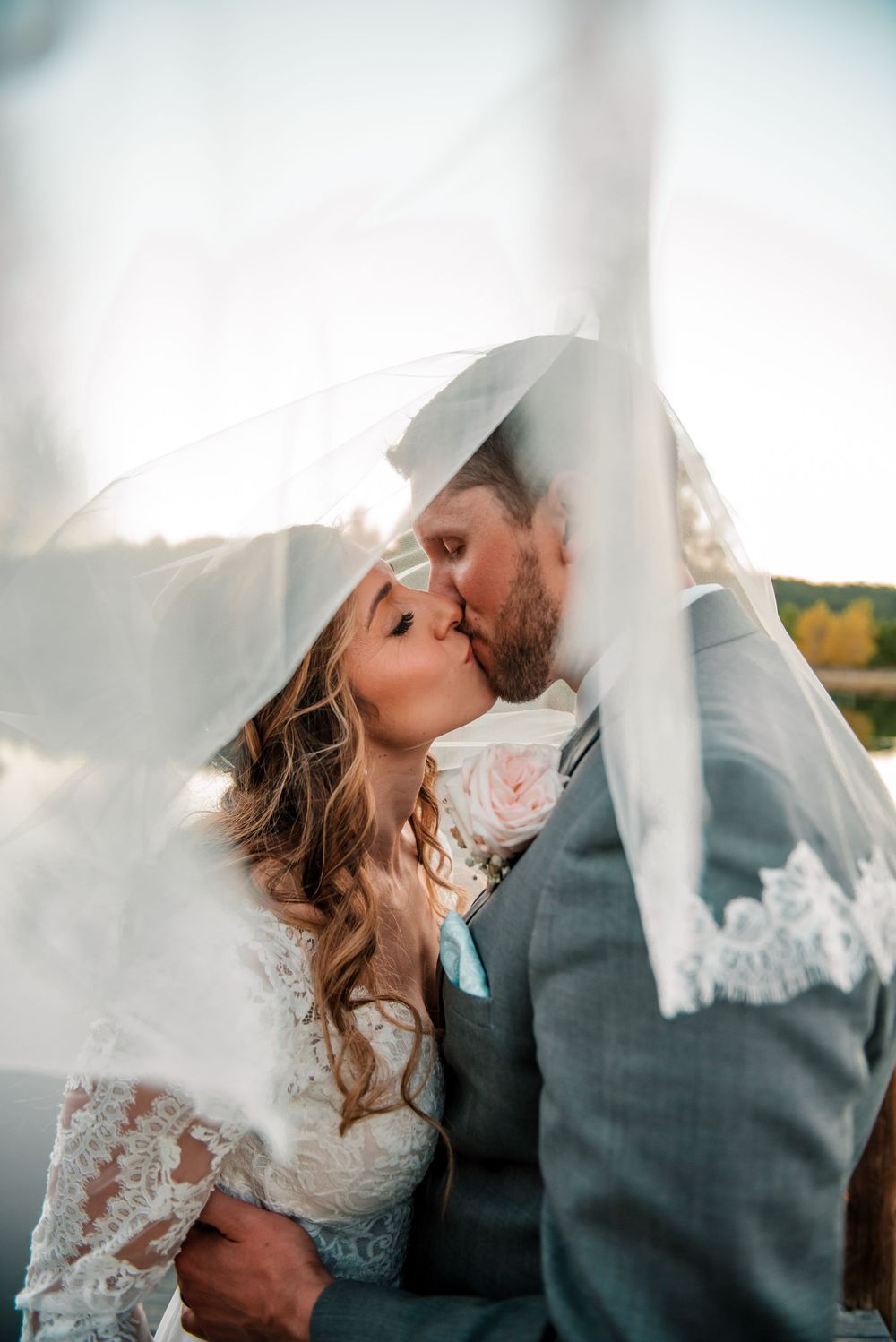 Romantic moment captured through sheer wedding veil at sunset.