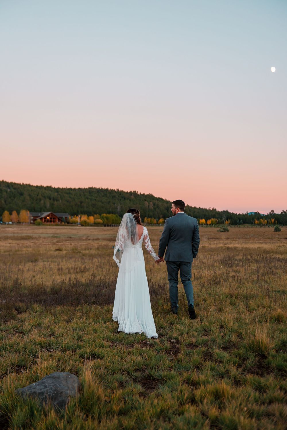 Couple walking through a golden meadow at dusk with mountains in the background.
