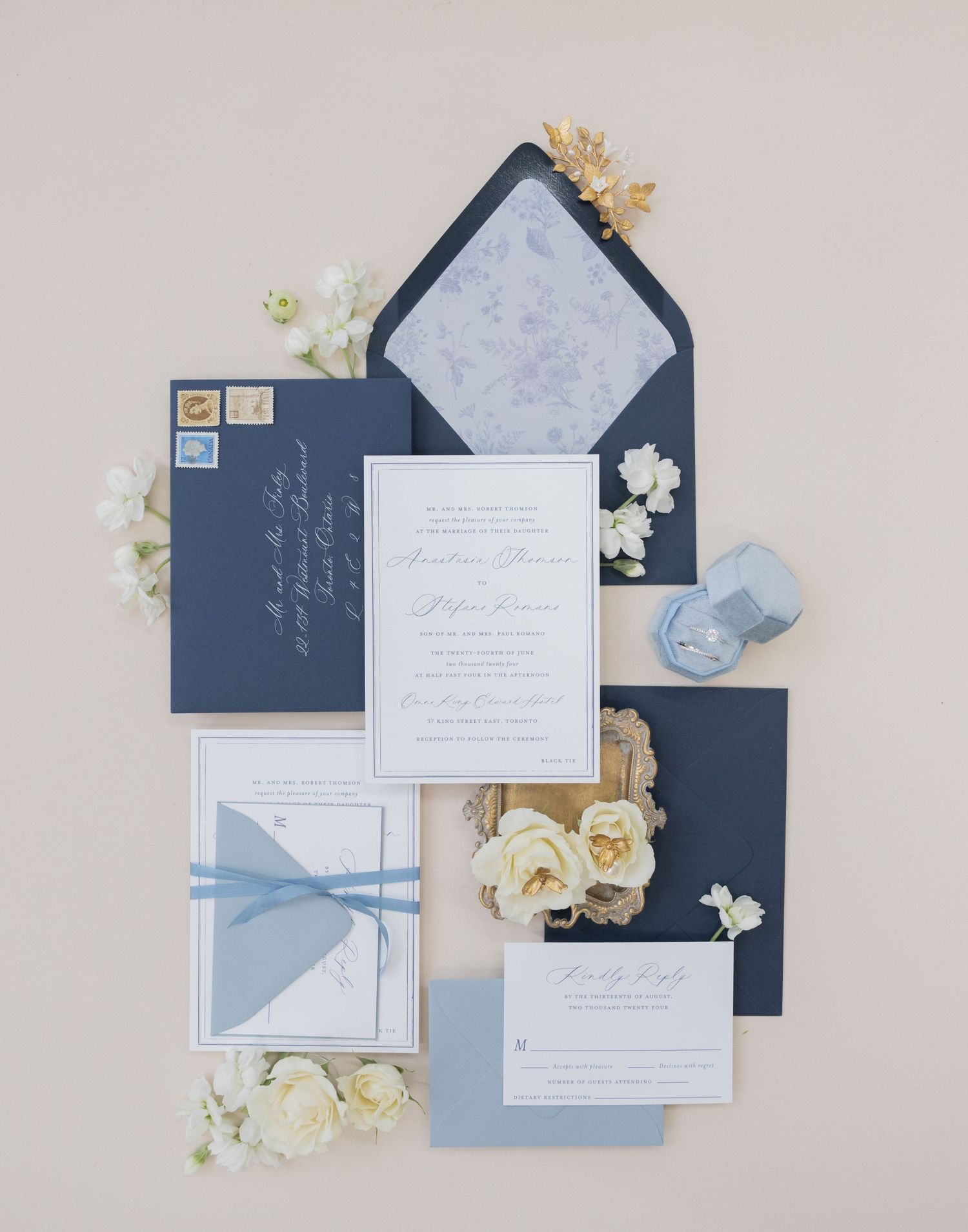 Navy blue and white wedding stationery flat lay with cream roses and light blue accents.