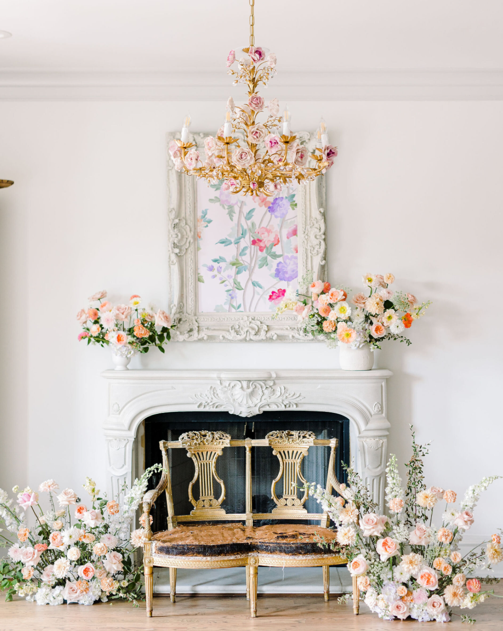 Elegant white fireplace mantel decorated with pink floral arrangements and gold accents.
