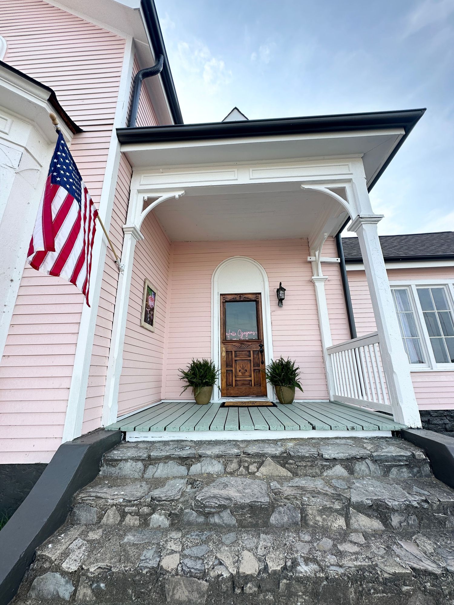 Pink church entrance with American flag, stone foundation, and white columns showing architectural details.
