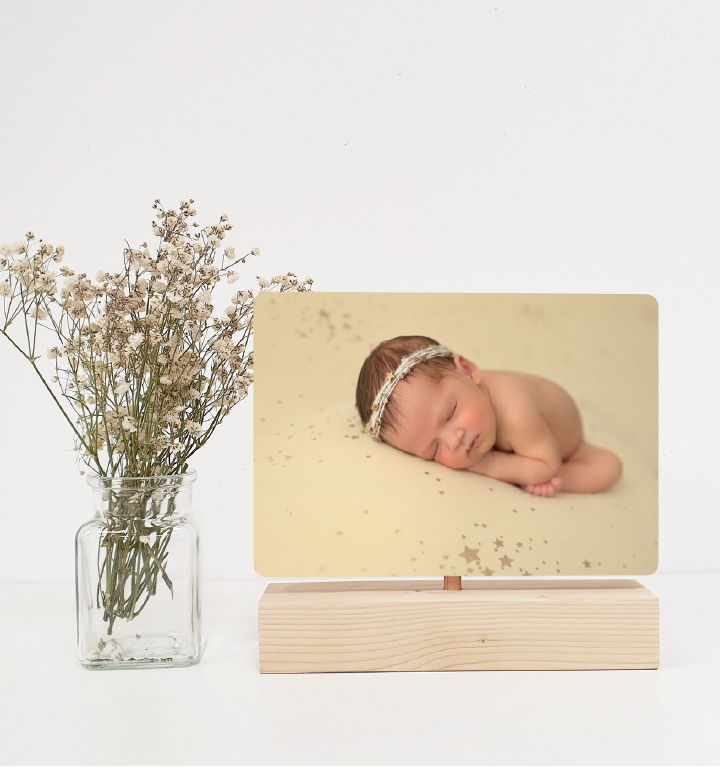 Professional newborn photo display with dried flowers in glass vase on white surface.