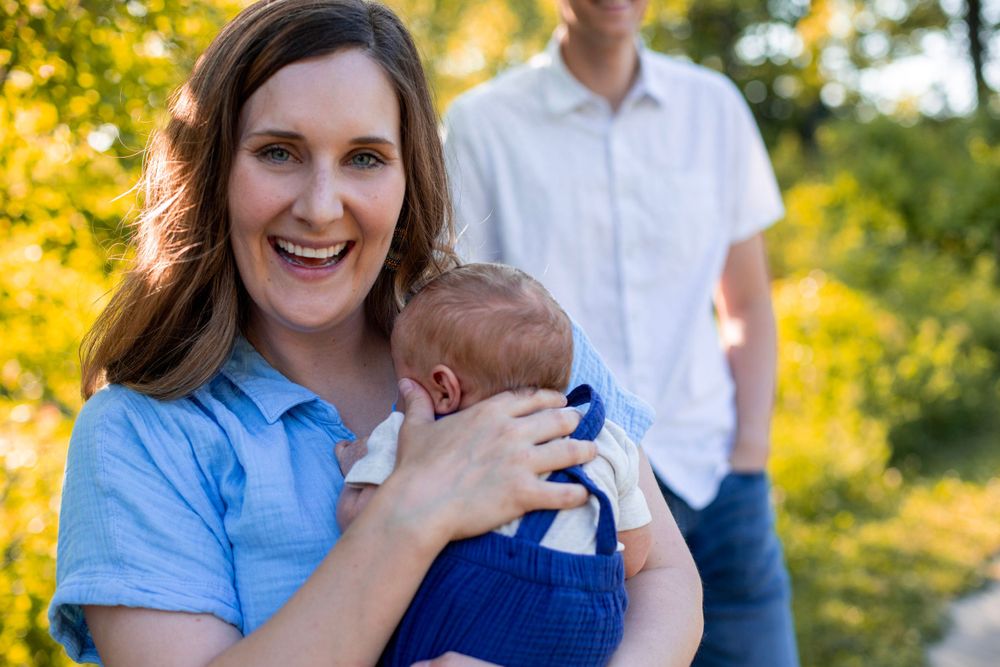 Sweet outdoor portrait of mother cradling newborn baby with golden bokeh background.