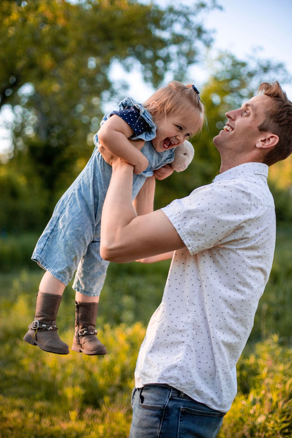 Playful outdoor moment captured during golden hour as toddler is lifted high in the air.
