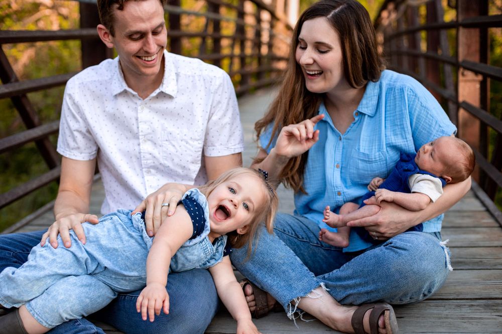 Family relaxing together on wooden bridge during outdoor photo session.
