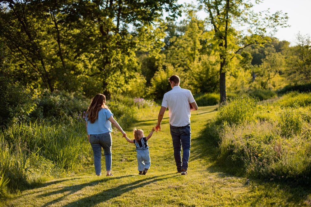 A family walks hand-in-hand down a nature trail surrounded by lush summer greenery.