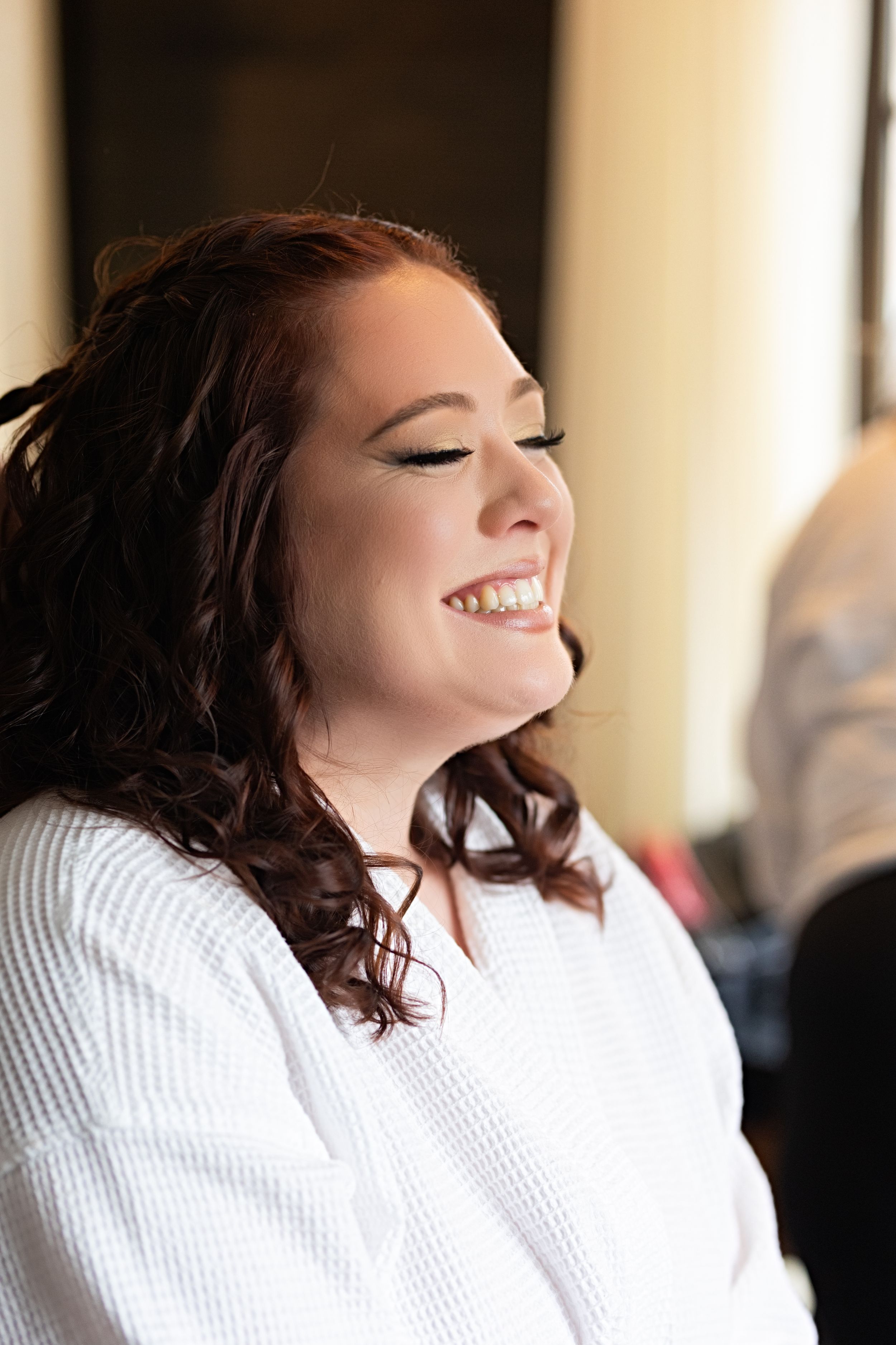 Radiant bride laughing joyfully in white robe while getting ready on her wedding day.