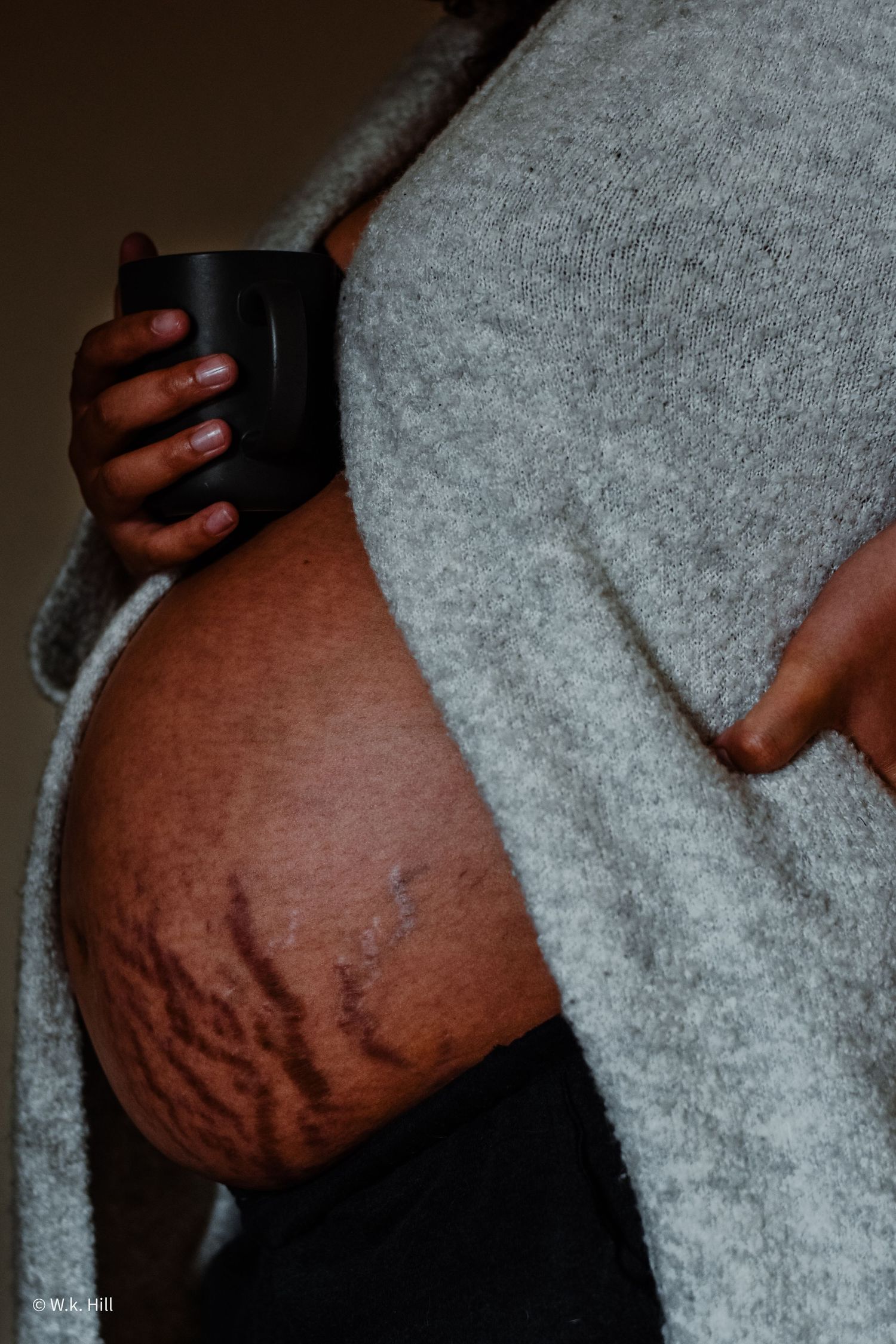 Close-up of a pregnant belly being cradled while holding a black mug.