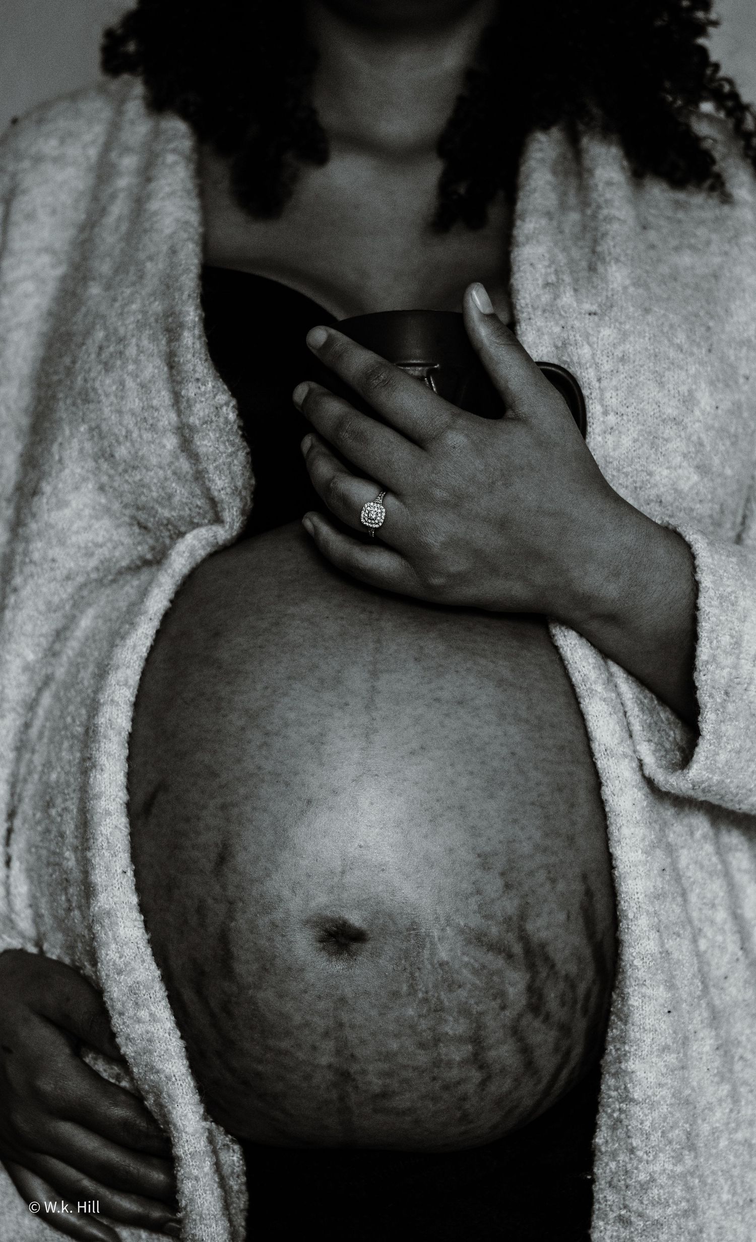 Black and white portrait of pregnant belly wrapped in towel with engagement ring visible.