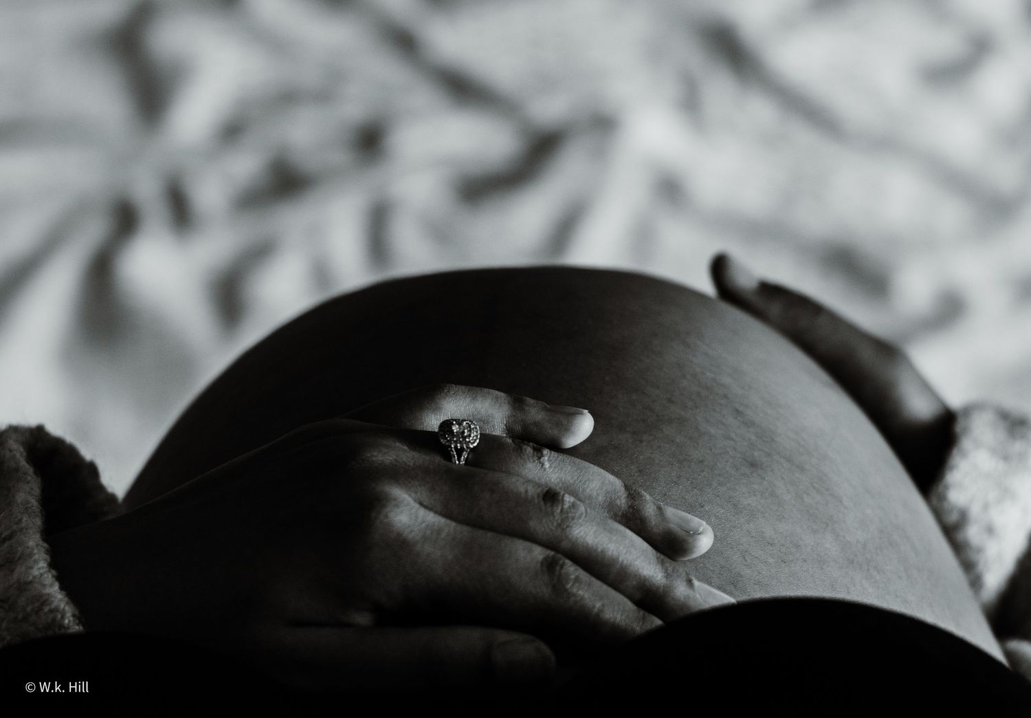 Silhouette of pregnant belly with hands resting on top in dramatic lighting.