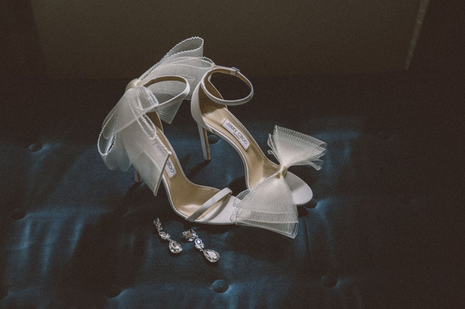 White wedding shoes with bows lie elegantly against a dark background.