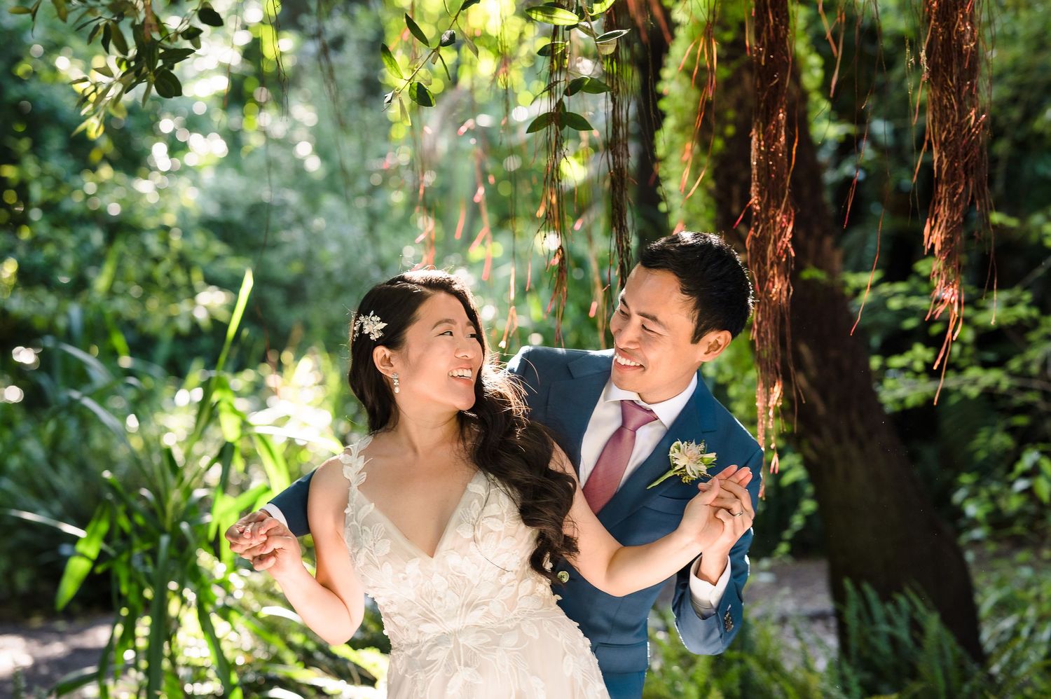 A joyful wedding moment captured in dappled sunlight among forest trees.