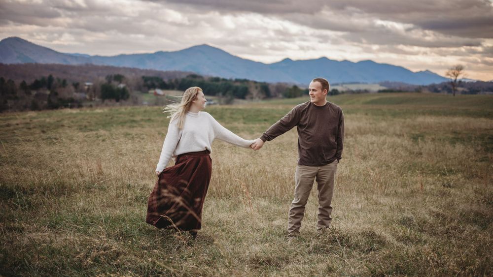 Couple walking together in mountain meadow under dramatic cloudy sky.