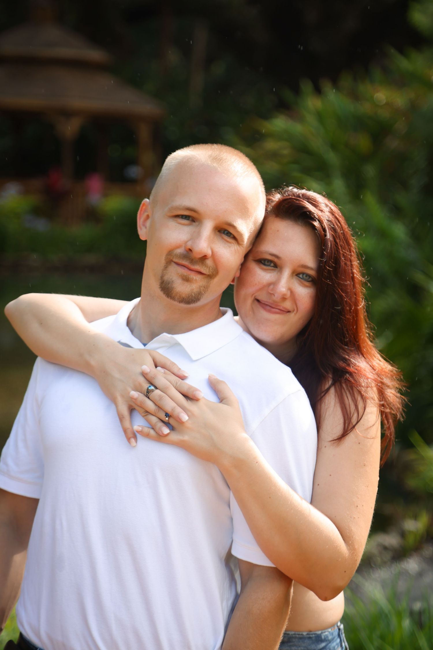 A romantic couple embraces outdoors in white shirts against a garden backdrop.