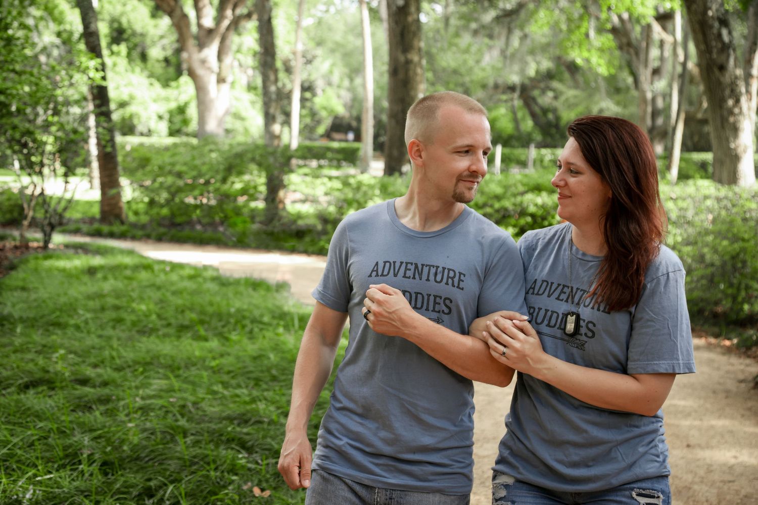 A couple wearing matching gray t-shirts share a playful moment in a park.