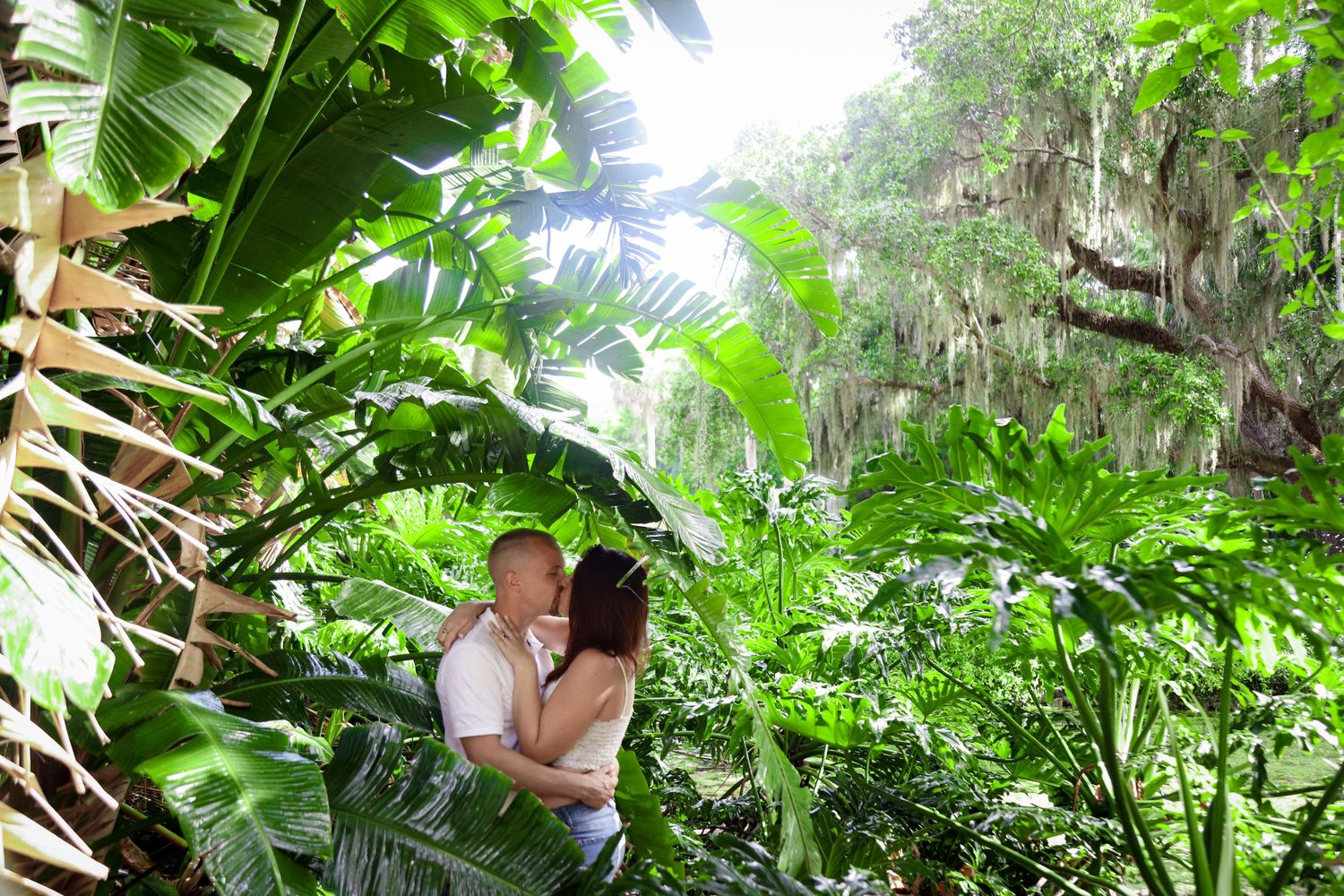 A couple shares an intimate moment surrounded by lush tropical foliage.