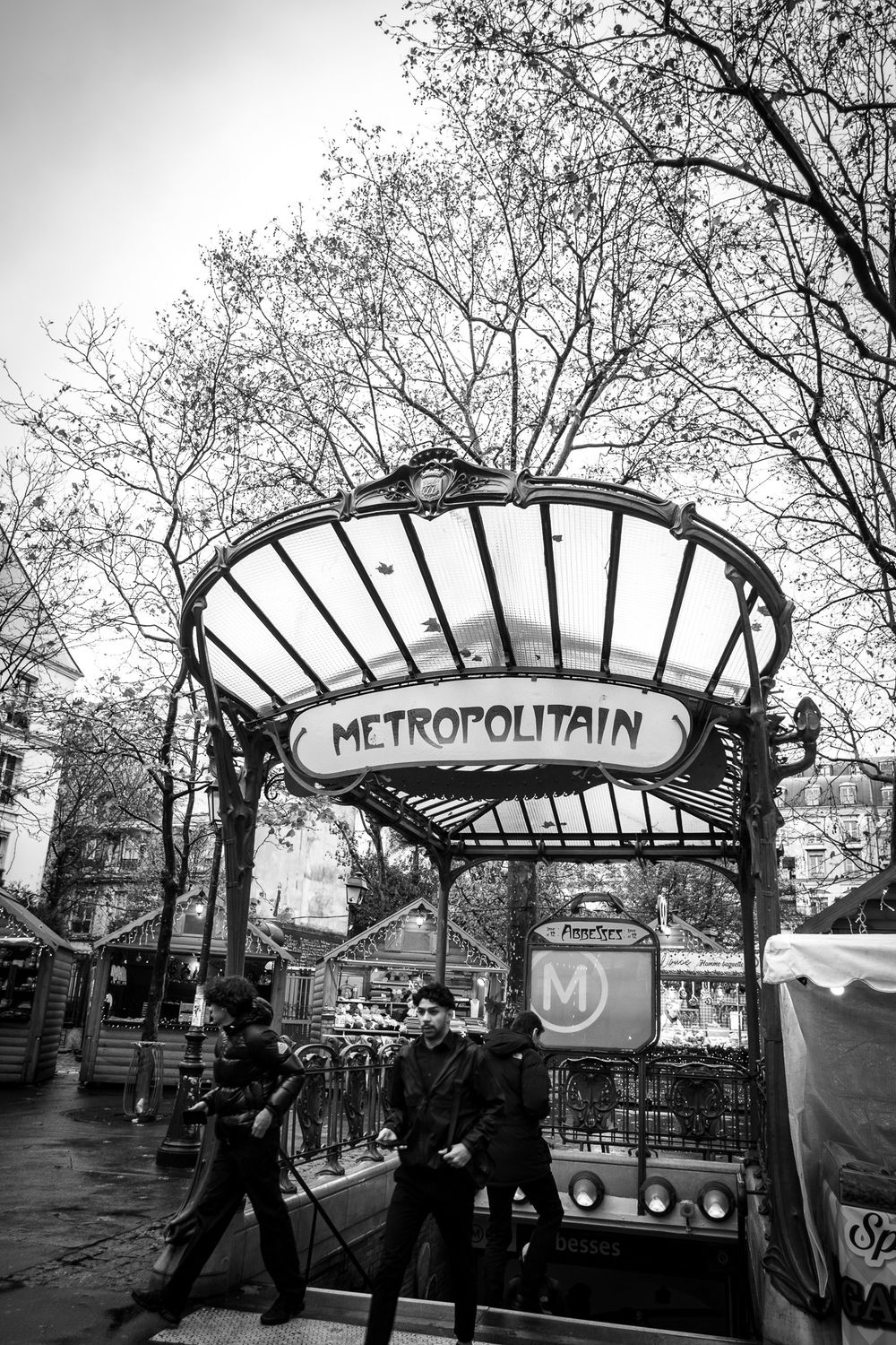 Black and white photo of iconic Art Nouveau Paris Metropolitain metro entrance with pedestrians passing by.