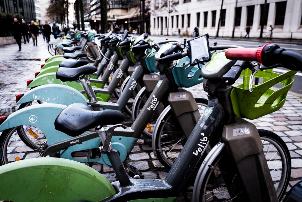 Row of green and black Velib public rental bicycles docked at a station on a Paris street.