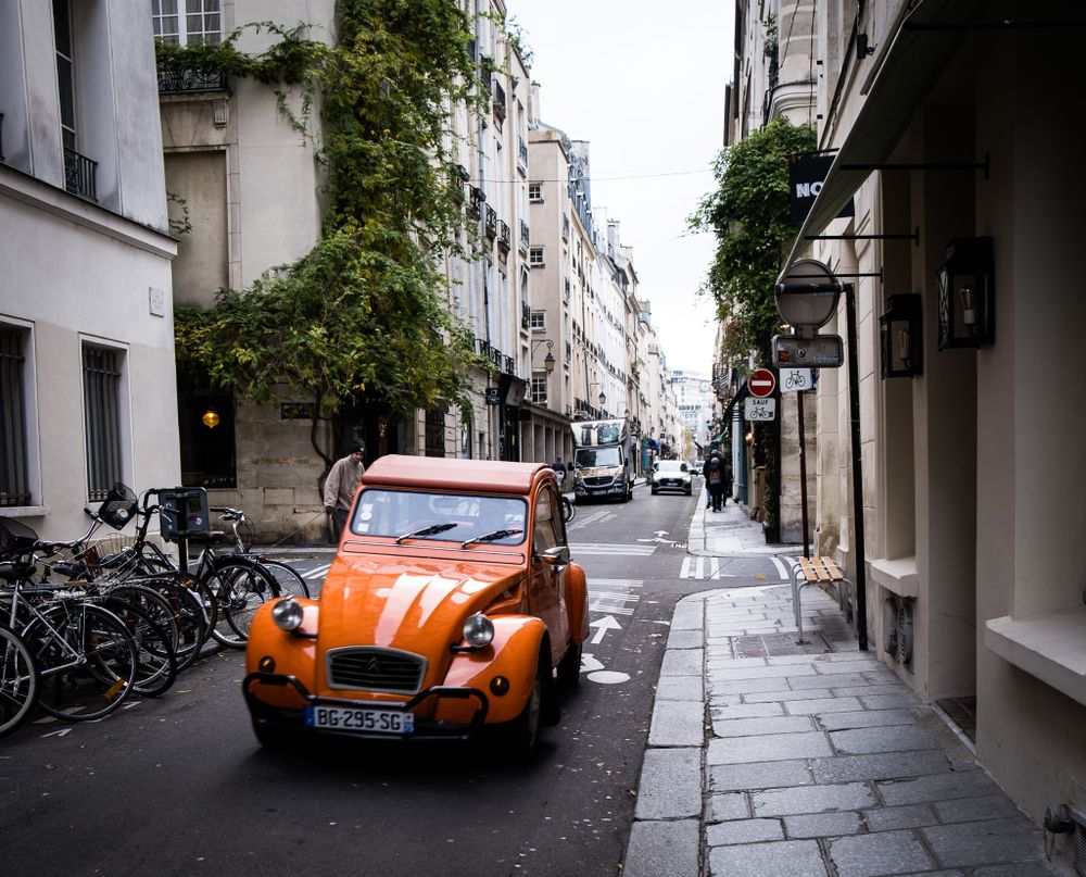 Vintage orange Citroen 2CV parked on a quiet narrow Parisian street lined with bicycles and buildings.