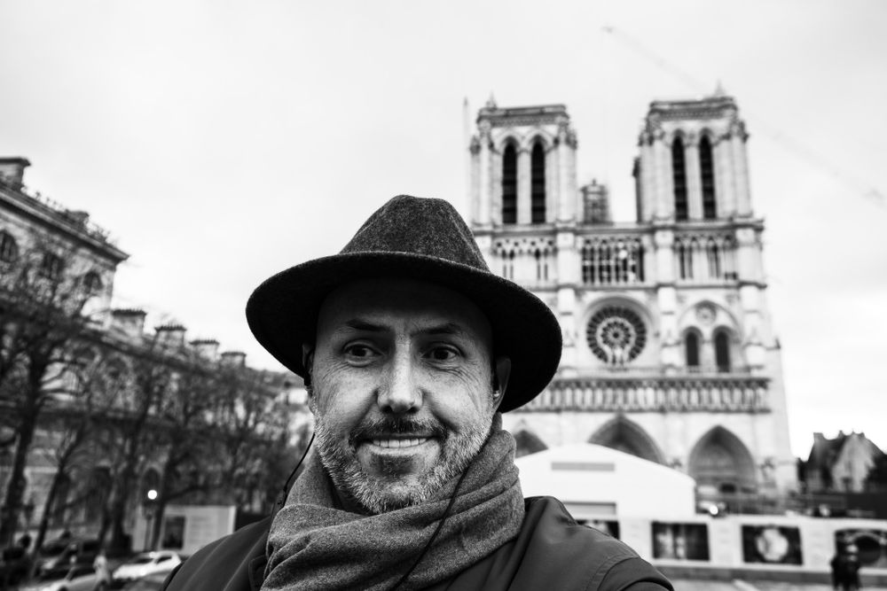 Man in hat smiling with Notre-Dame Cathedral Paris in background black and white photo.