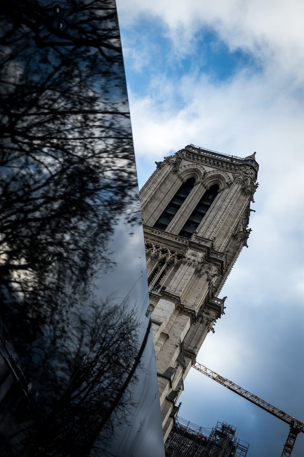 Dramatic low angle view of Notre-Dame Cathedral bell tower reflecting on glass surface Paris.
