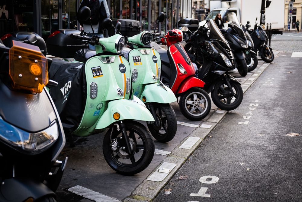 Colorful scooters and mopeds parked in a row on a Paris city street.