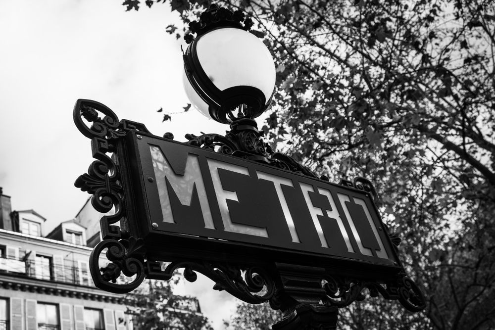 Vintage black and white Paris Metro sign with ornate ironwork and street lamp.
