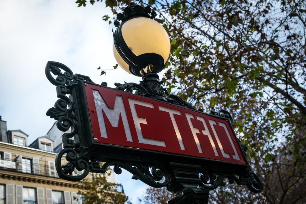Classic red Paris Metro sign with ornate black ironwork and glowing street lamp.