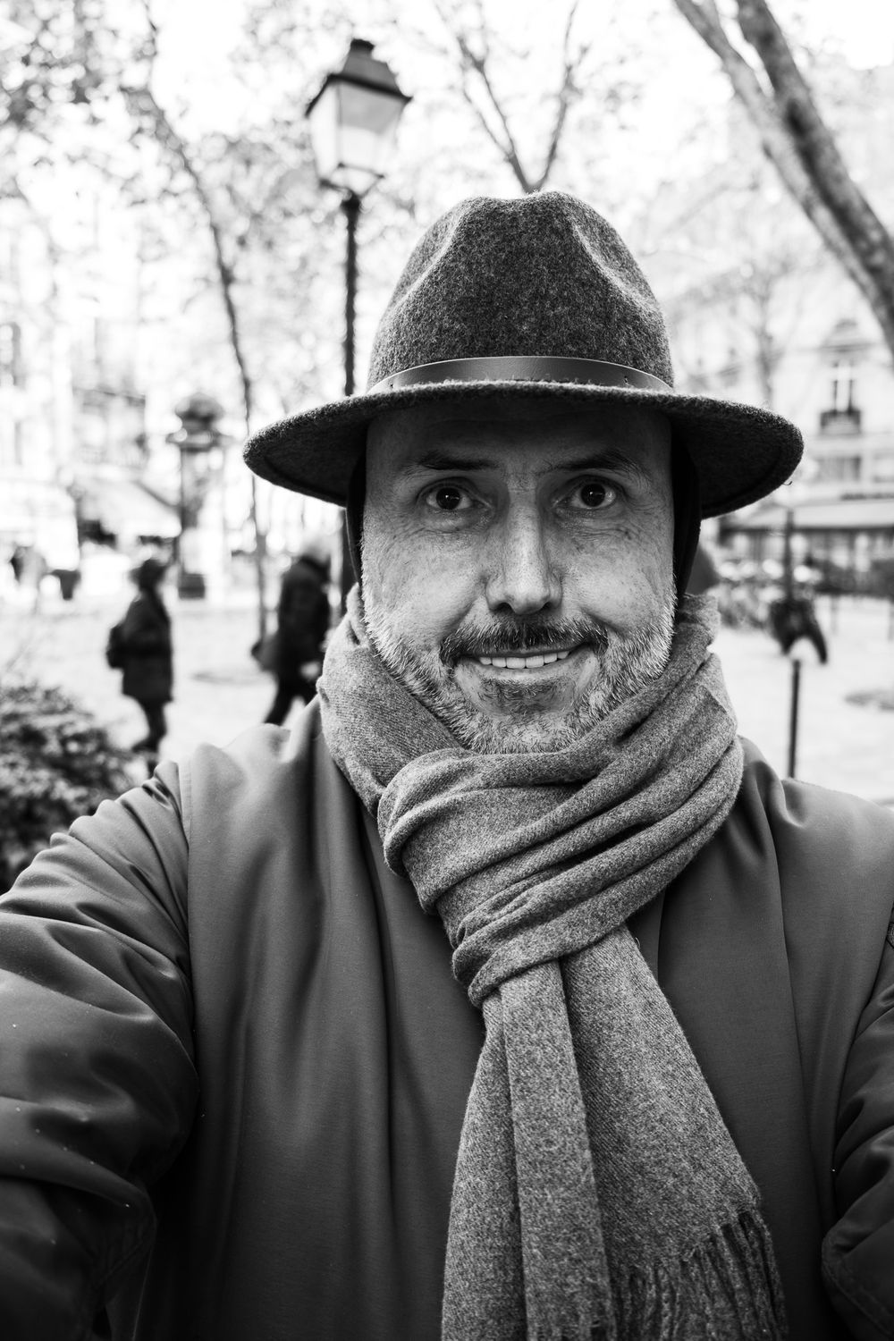 Black and white portrait of bearded man in fedora hat and scarf on Paris street.