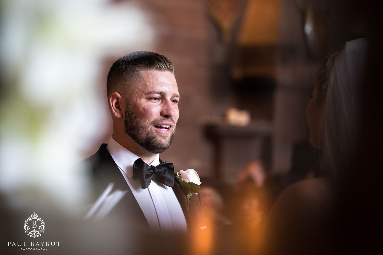 Close-up wedding portrait of groom in tuxedo and bow tie with soft focus background.