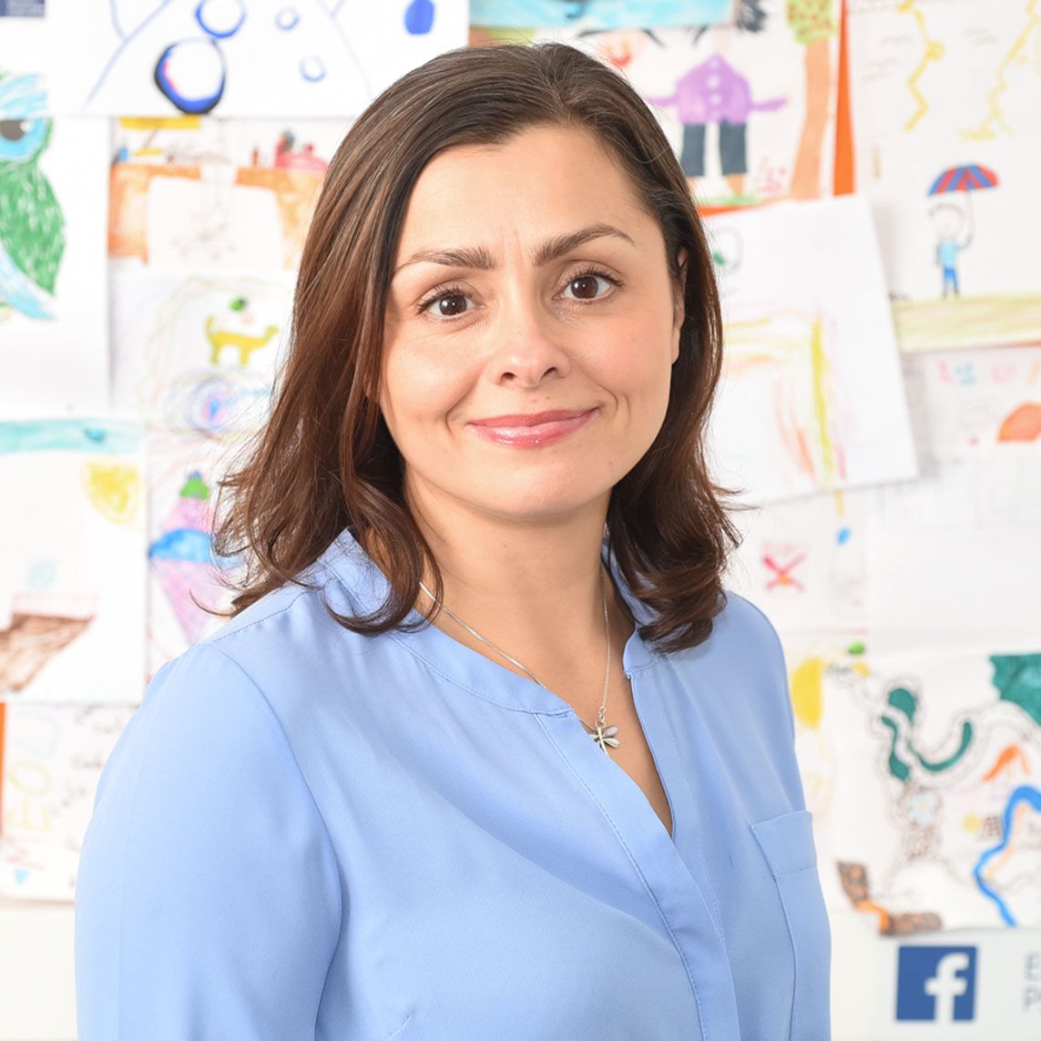 Dr. Lucy Russell, a child psychologist, poses in a blue shirt in front of a picture wall, captured by Abigail's Studio.