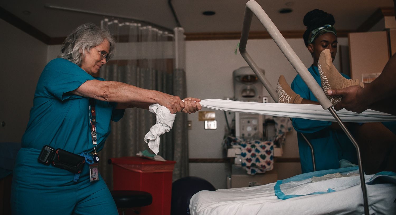 doctor holding sheet with pregnant woman in hospital bed tug of war