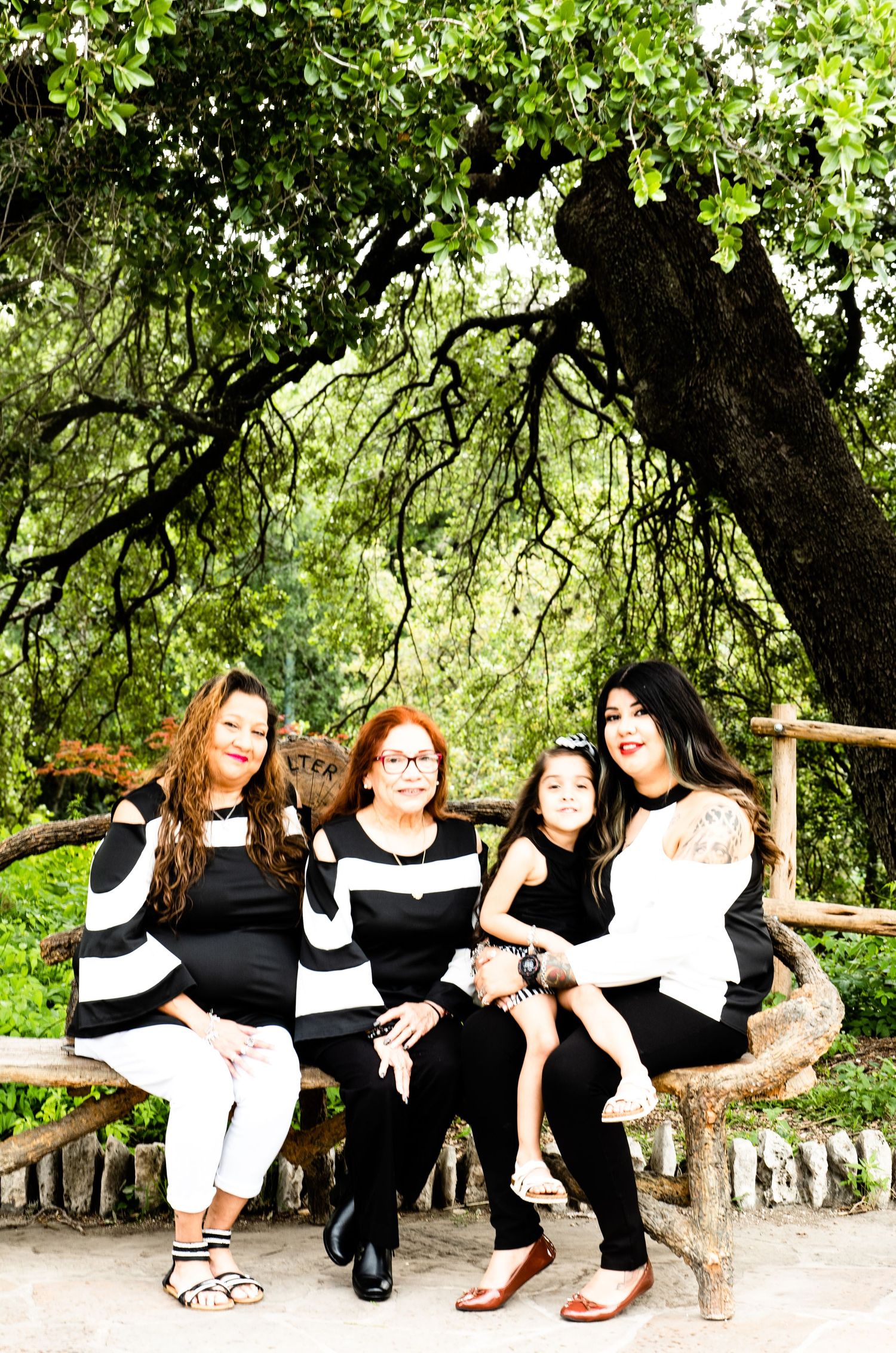 Portrait of 4 generations pose together on a rustic wooden bench surrounded by lush greenery al the Japanese Tea Gardens.