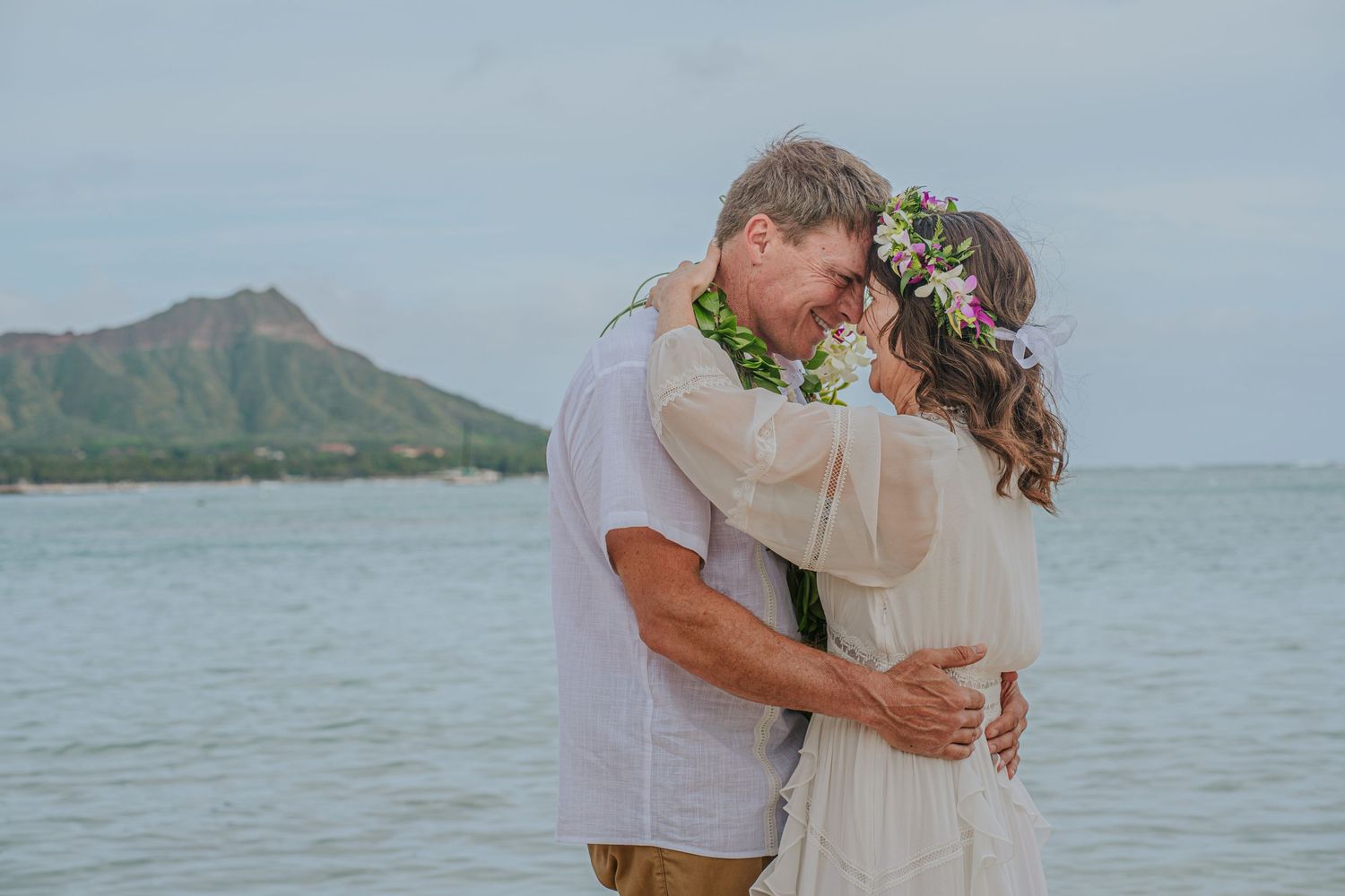 Romantic moment captured on beach with Diamond Head crater visible in distance.
