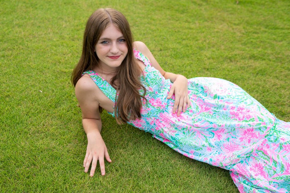 Person in a floral print summer dress laying on green grass in a casual outdoor pose.