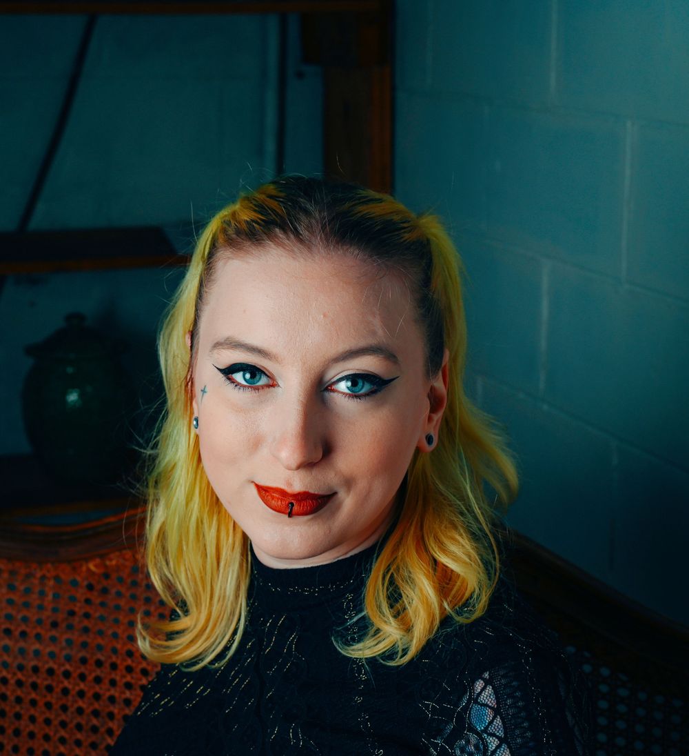 Portrait against turquoise wall features bold red lipstick and blonde hair with dramatic makeup.