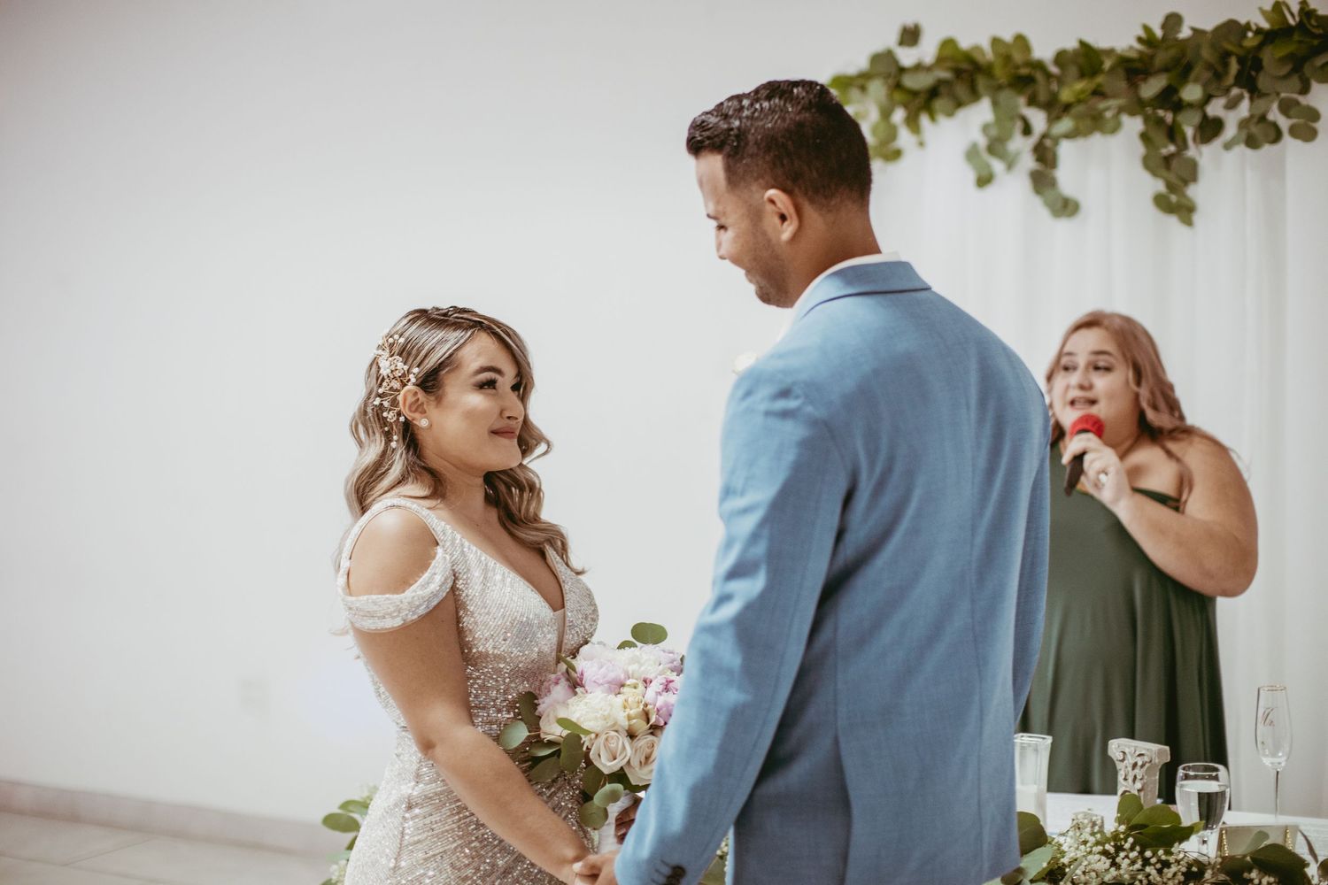 Wedding ceremony scene with couple and officiant under hanging greenery decoration.