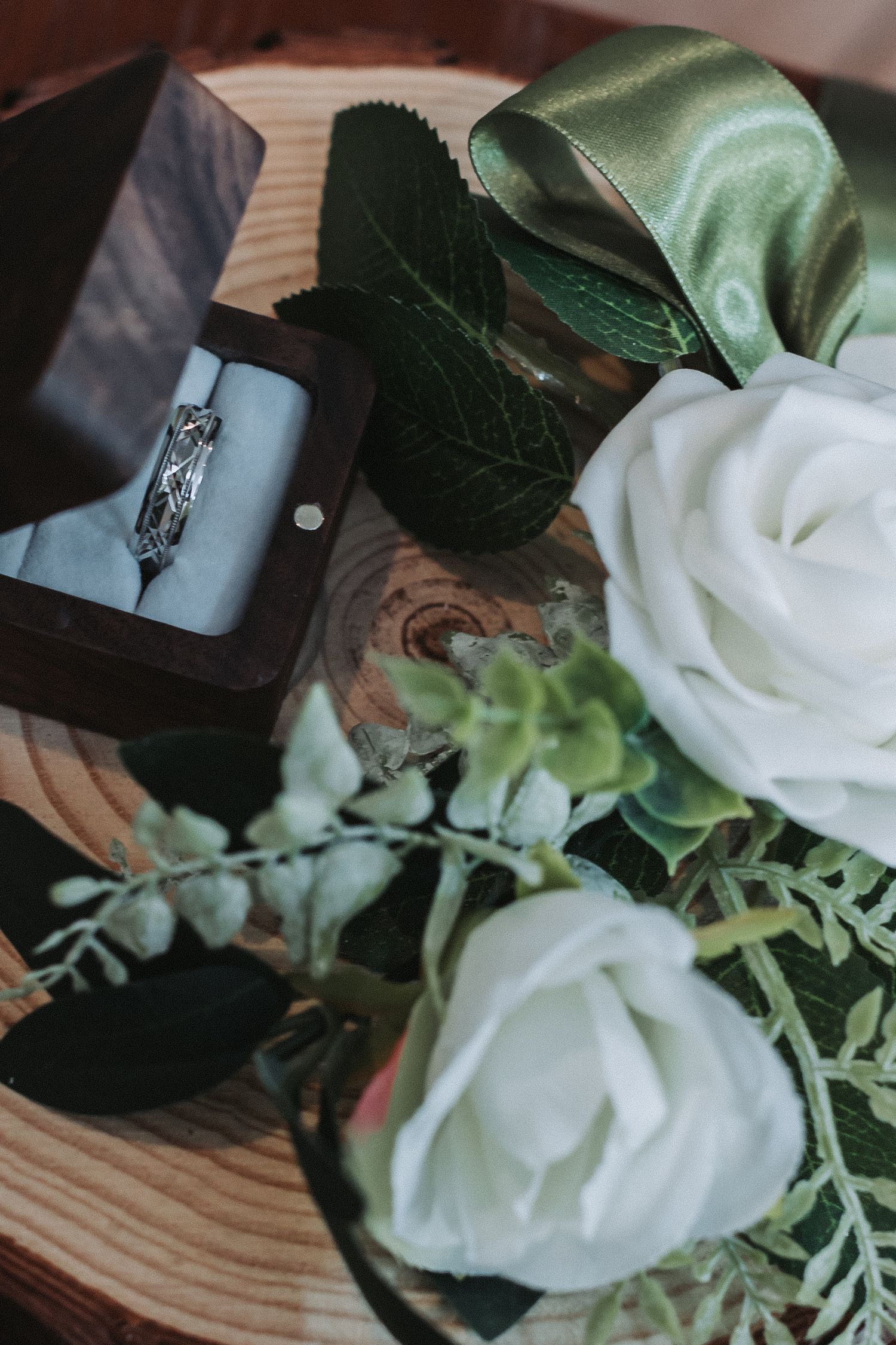 An engagement ring in a box surrounded by white roses and greenery.