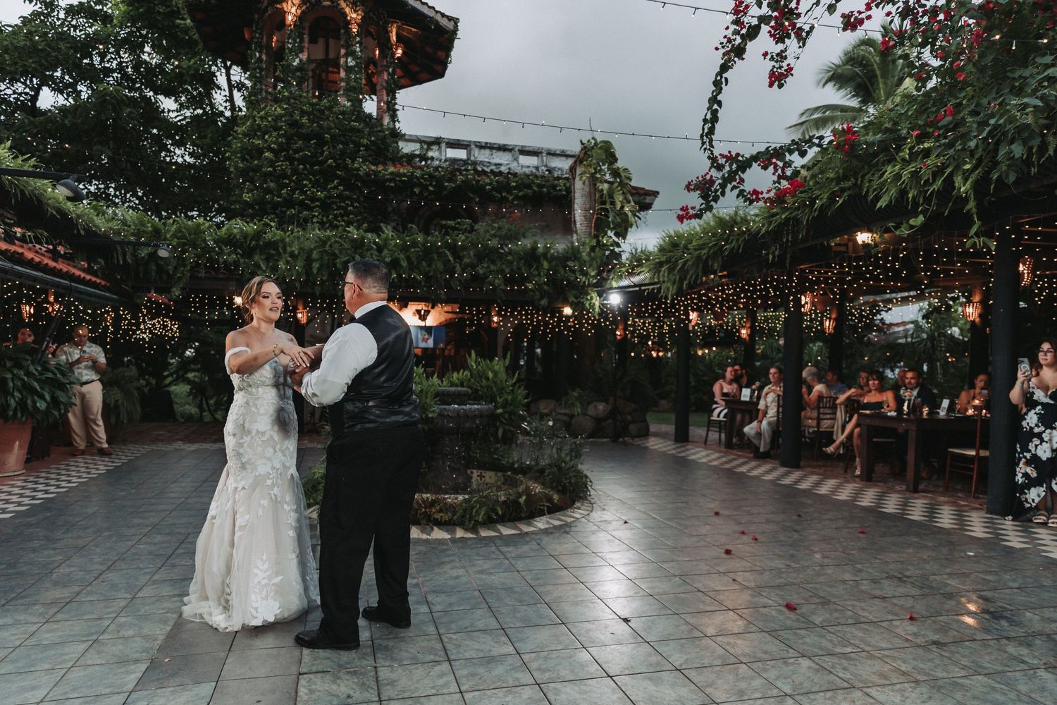 A couple shares their first dance at an outdoor reception venue with string lights.