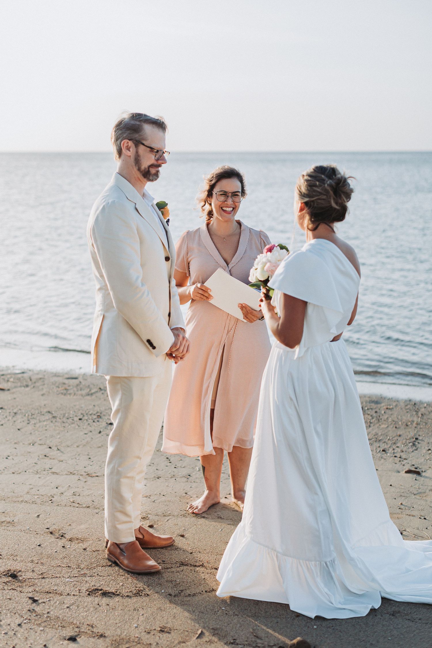 A beachside wedding ceremony with attendees in light summer attire against an ocean backdrop.