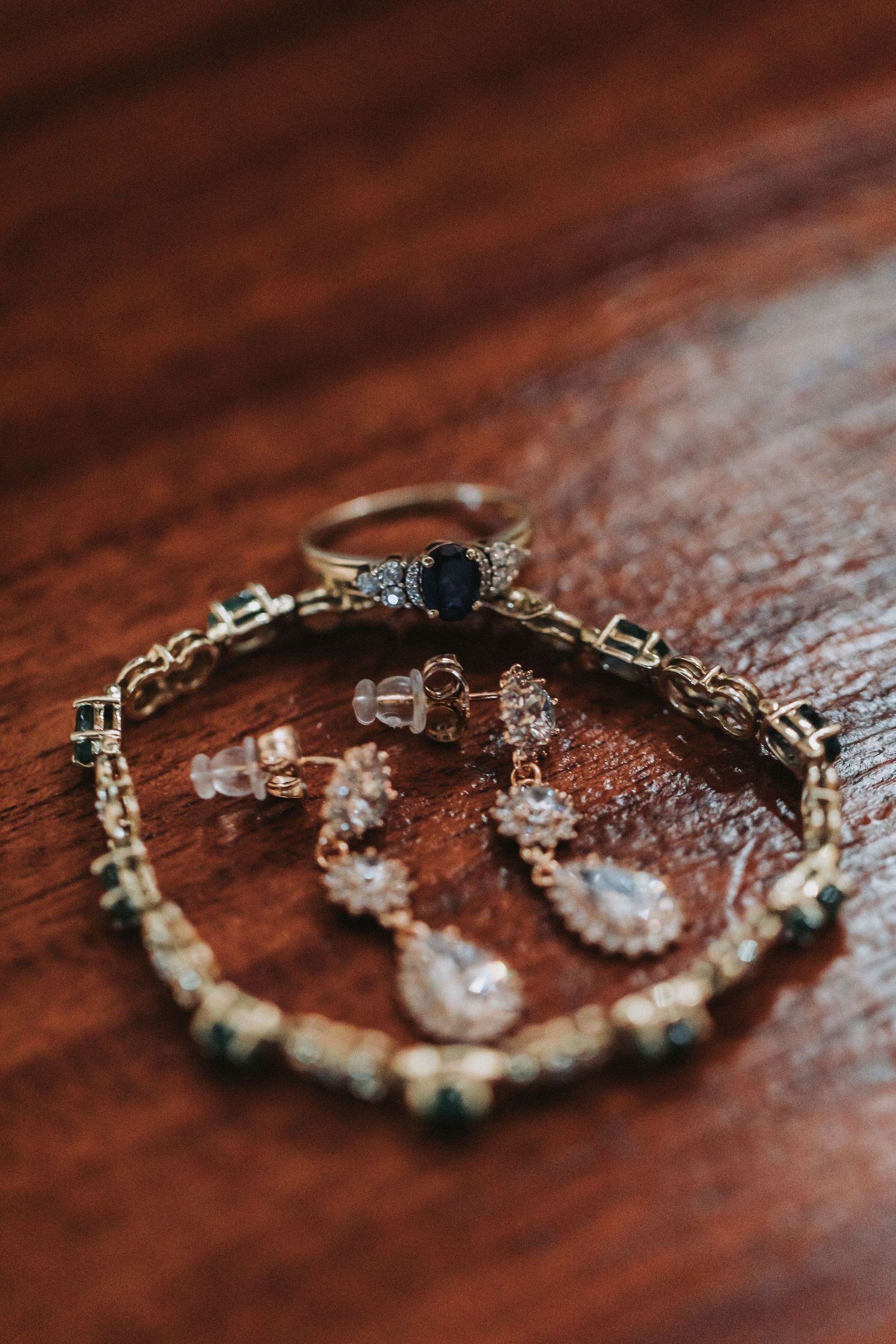 Elegant wedding jewelry including a sapphire ring and crystal earrings displayed on a wooden surface.
