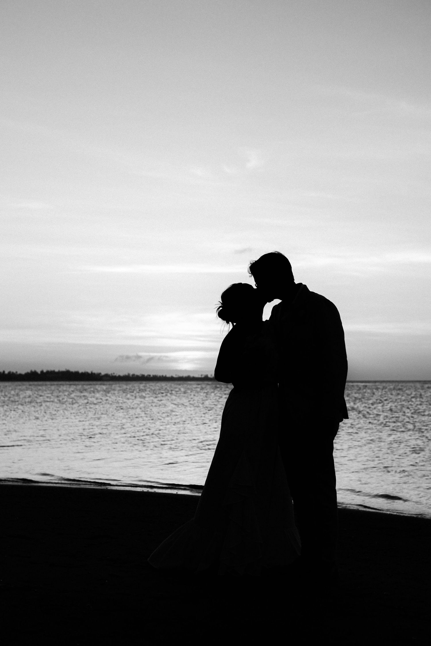 Romantic silhouette of a couple embracing on a beach at sunset against a moody sky and ocean backdrop.