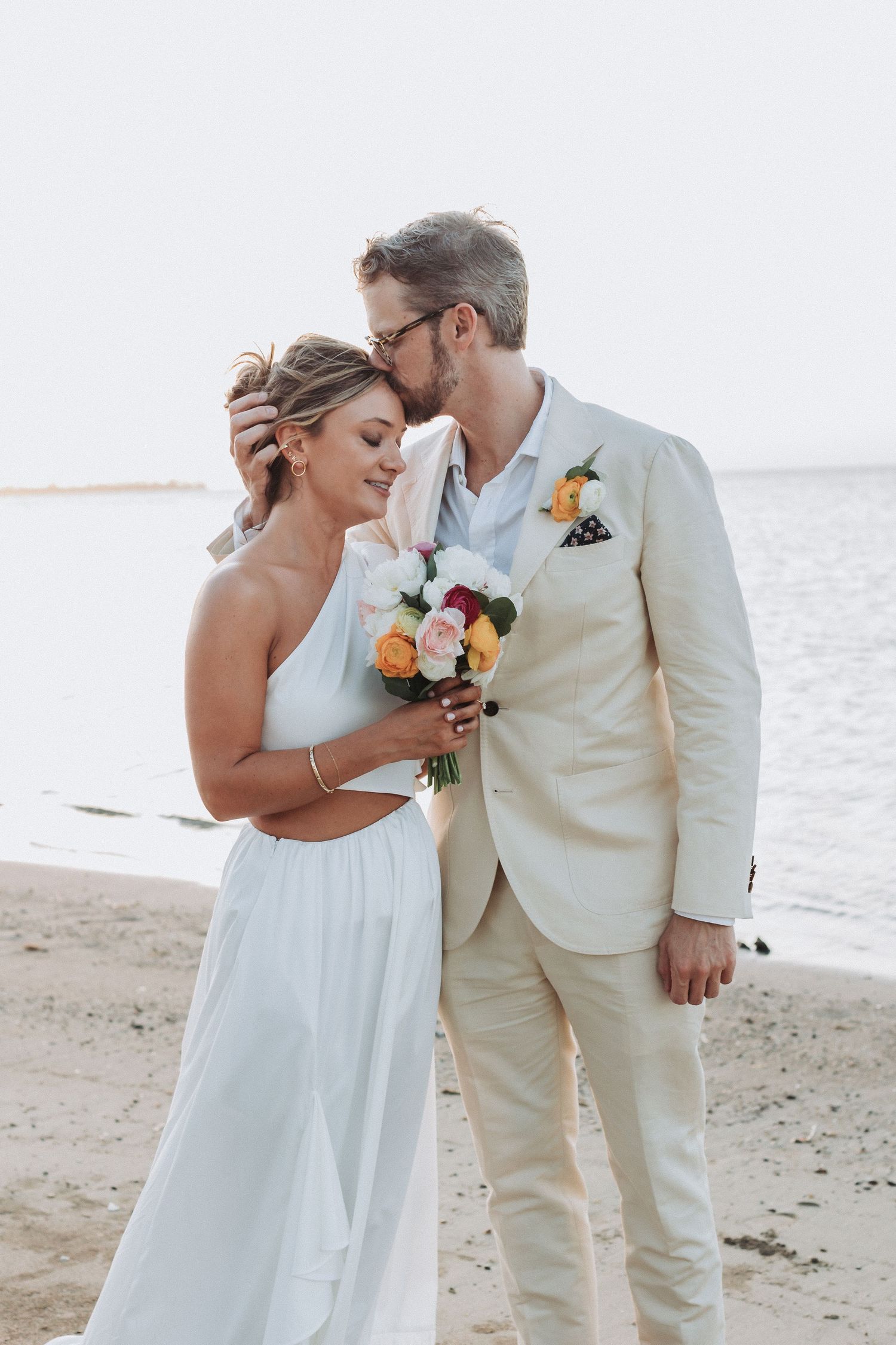 A romantic beach wedding portrait with couple in white and cream formal attire.