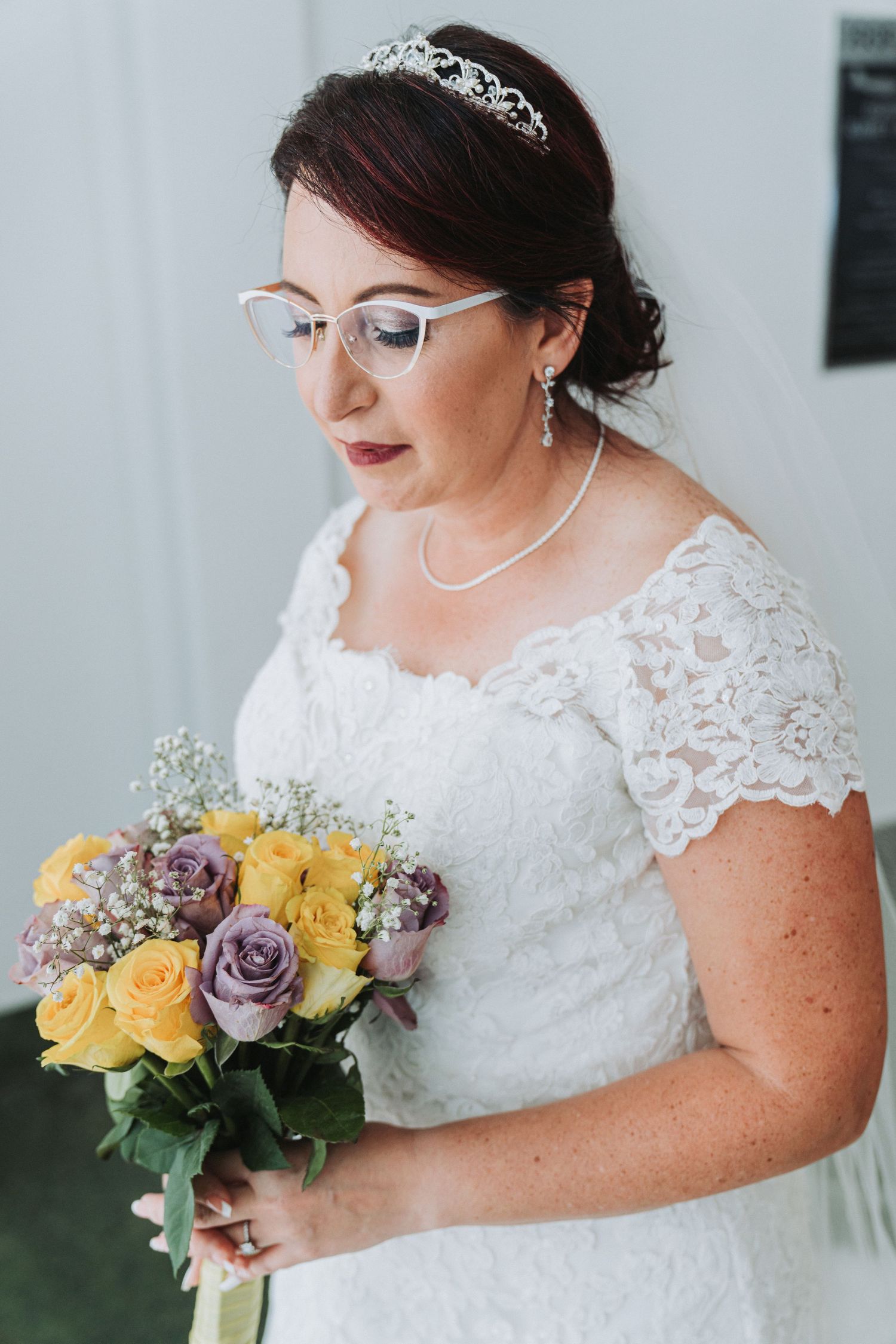 Beautiful bridal portrait featuring a lace wedding dress, tiara, and bouquet with yellow and purple flowers.
