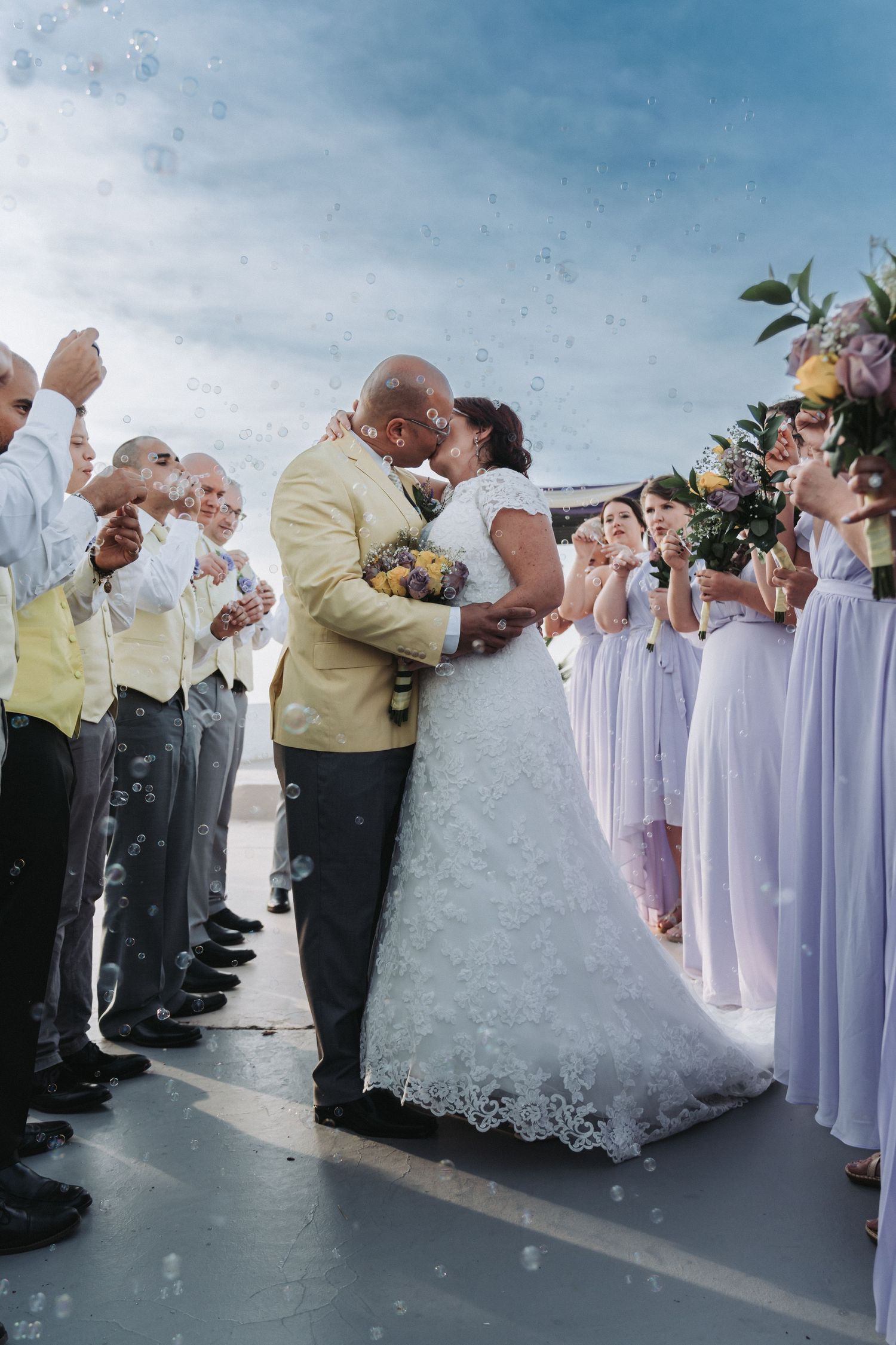 Wedding ceremony celebration with attendants in lavender and yellow while bubbles float through the air.