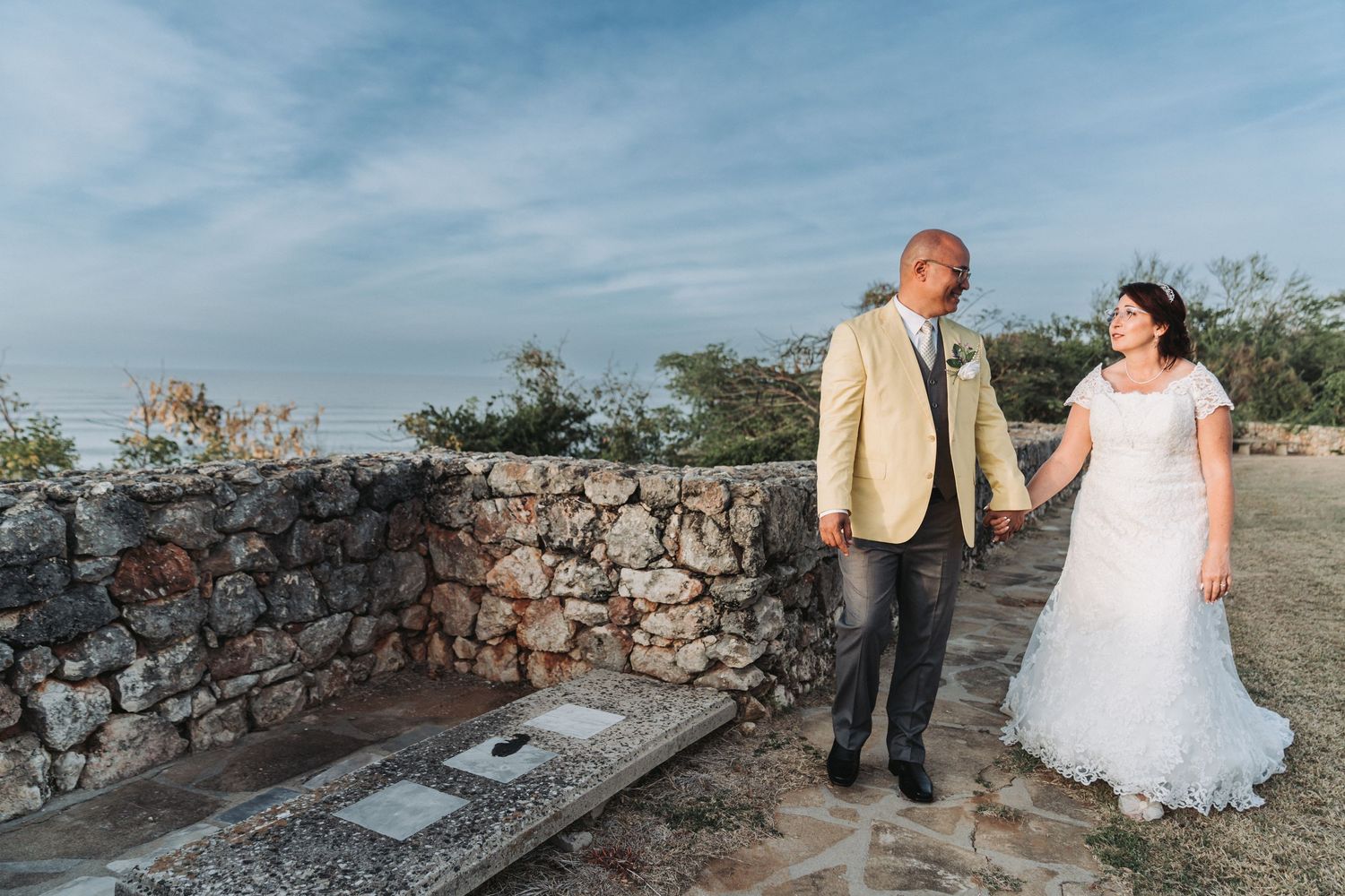 Romantic coastal wedding portrait with stone wall and ocean backdrop.