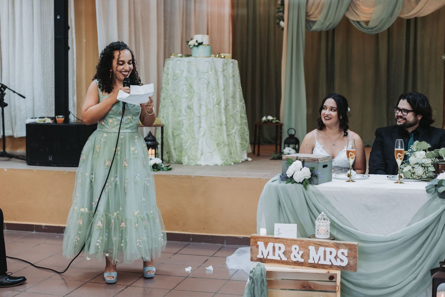 A toast is given at an elegant wedding reception with mint green decor and a "Mr & Mrs" sign displayed at the head table.
