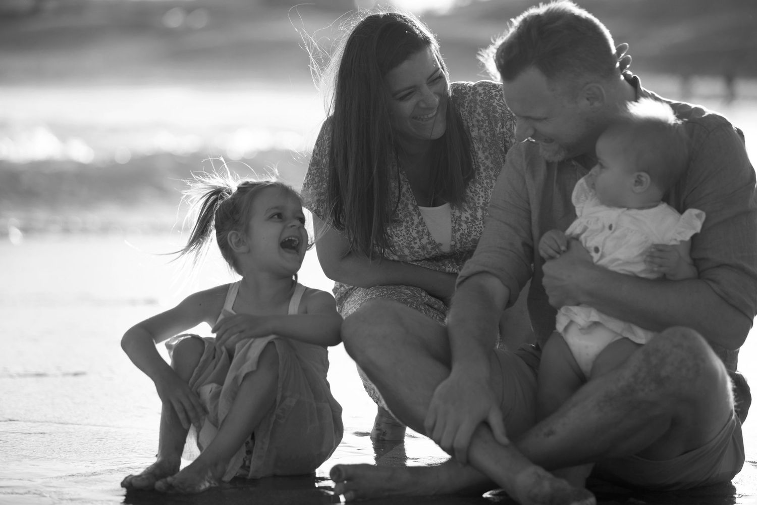 Black and white portrait of a family sharing a tender moment outdoors at sunset.