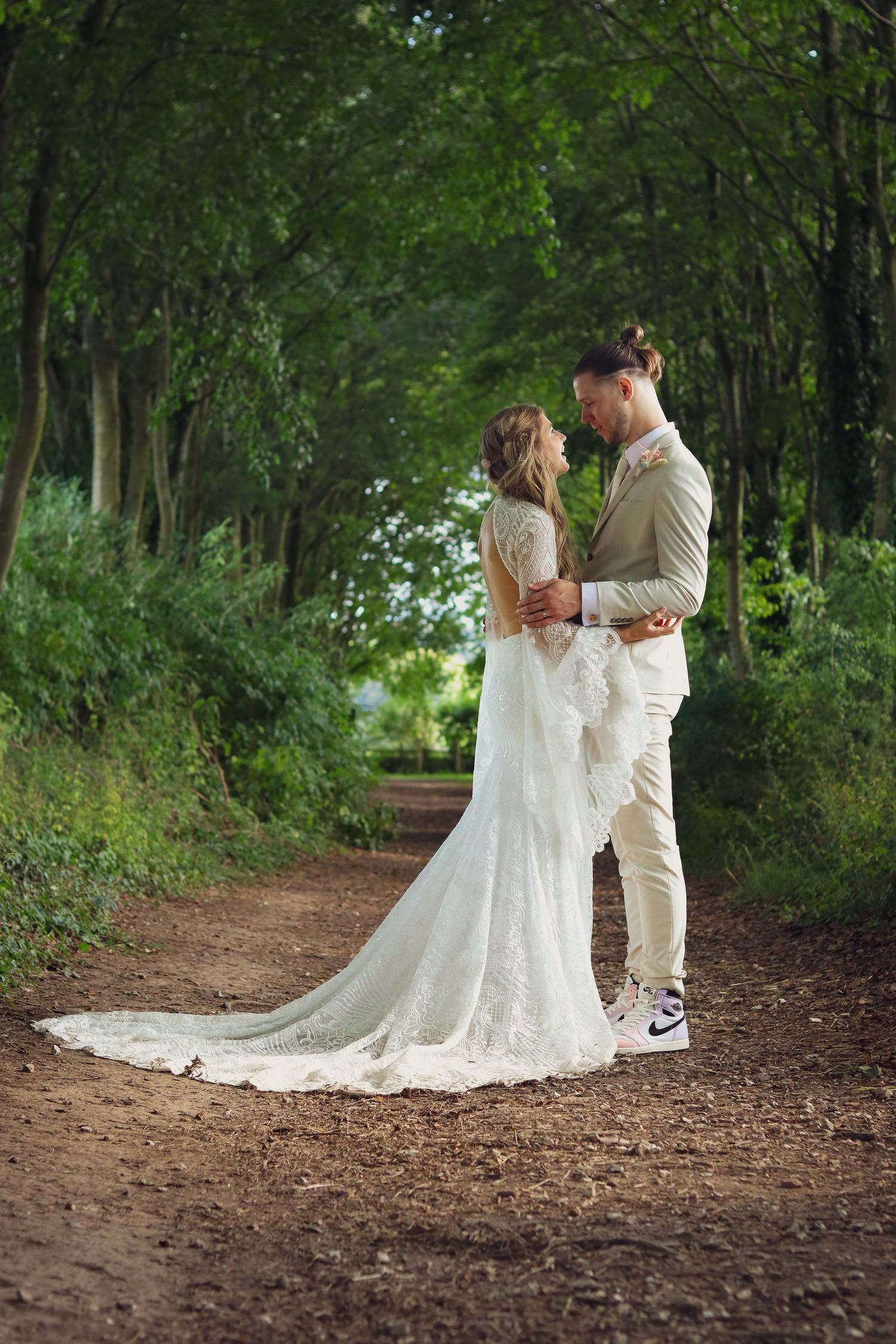 Wedding couple in elegant attire share intimate moment on forest path.